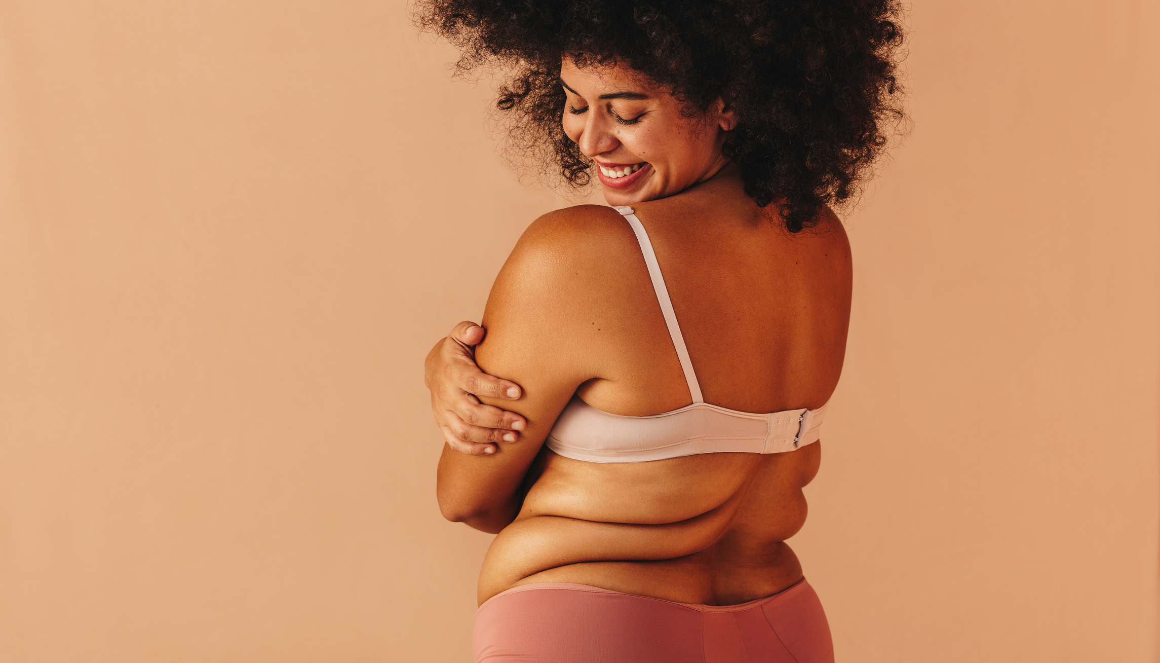 Self-loving plus size woman smiling happily while wearing underwear. Body positive woman with an Afro hairstyle embracing her natural body and curves.
